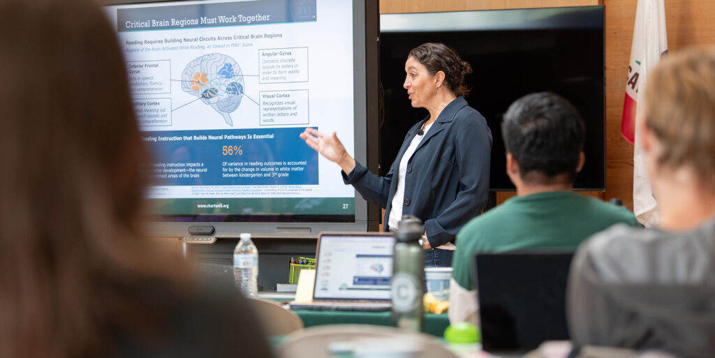 Presenter Chantel Touryan-Schaefer talking to attendees with a slide on critical brain regions displayed behind her.